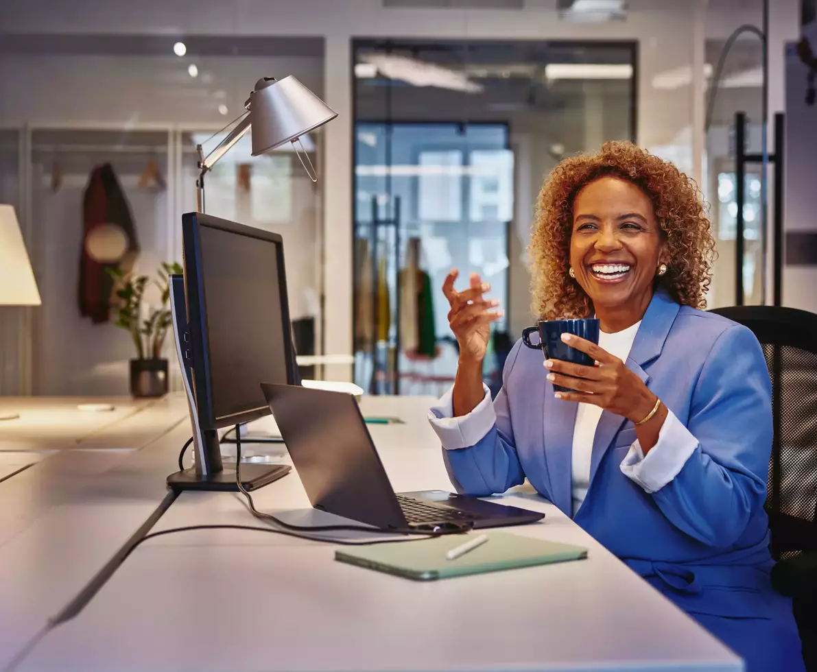 Female with blue blazer sitting behind computer at a desk, smiling to a person